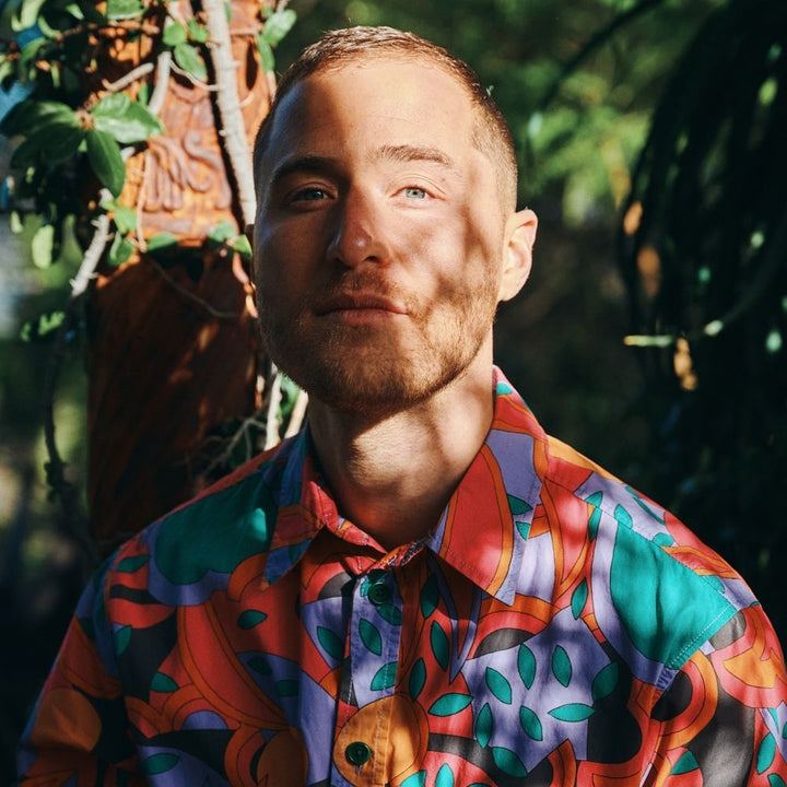 Mike Posner in a colorful shirt among green leaves